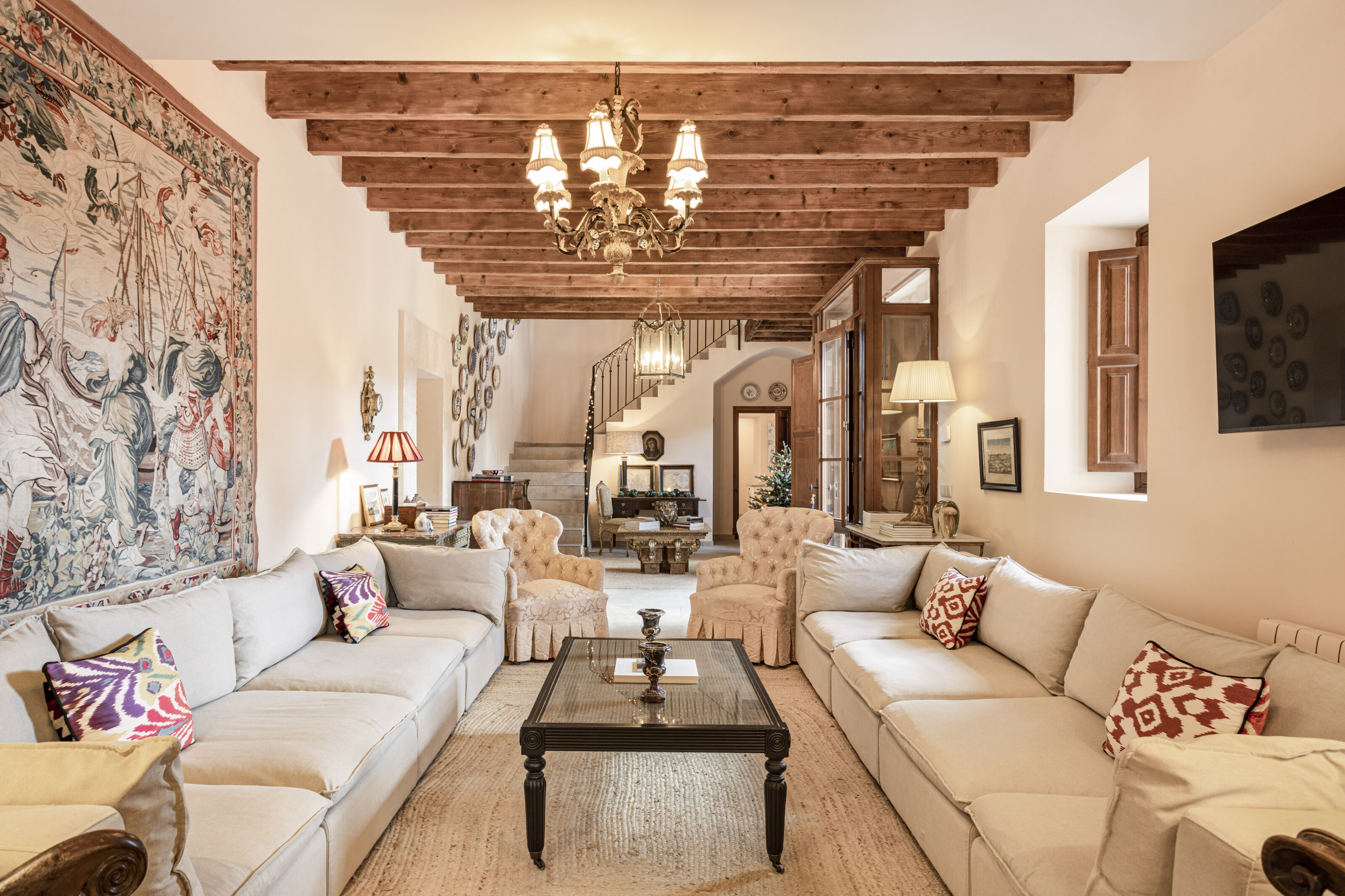 A light-filled sitting room with timber beams, antique chairs and a wall tapestry